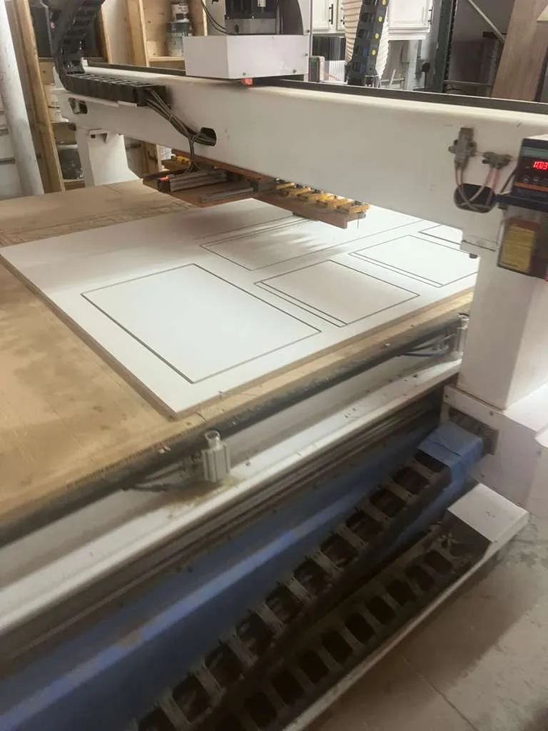 CNC router with shaker door profiles cut into a white panel