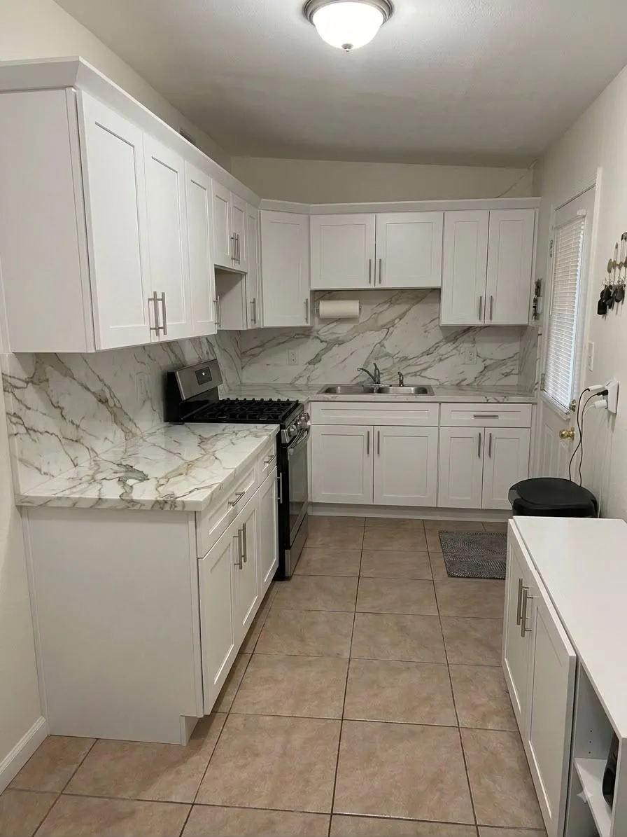 White galley kitchen with marble-look slab backsplash. A Yoll Remodeling job in Orlando and Central Florida